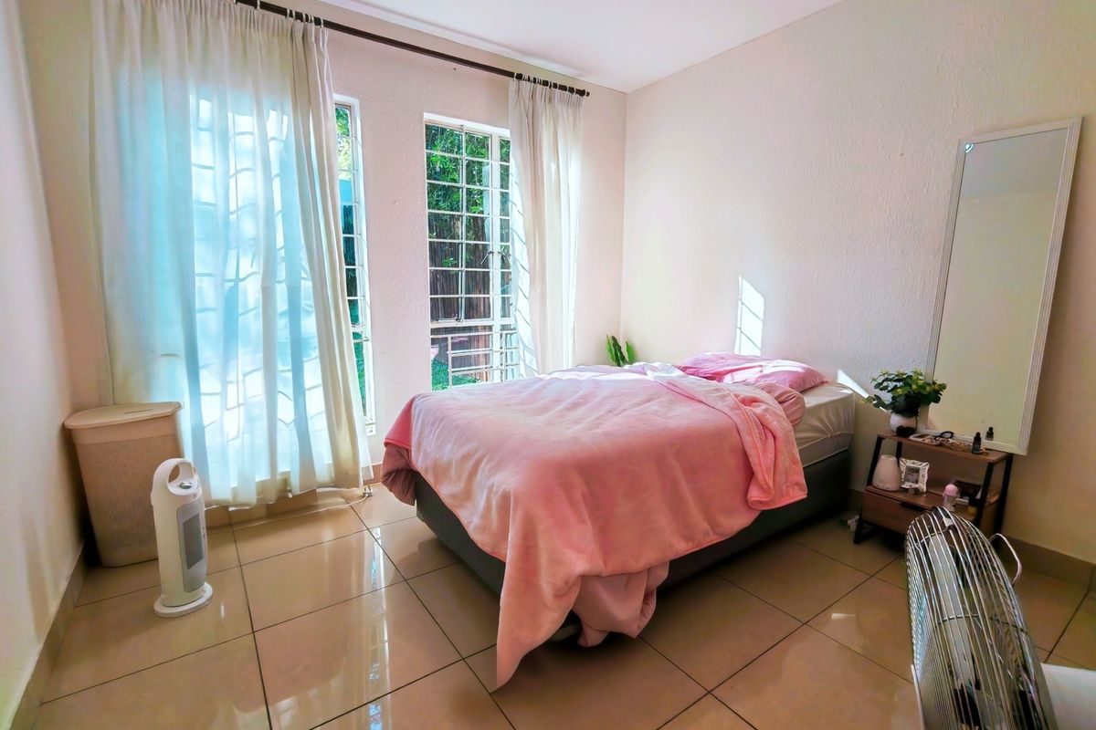 A bright bedroom featuring large windows with natural light, tiled flooring, and neutral wall finishes, offering a clean and comfortable living space.