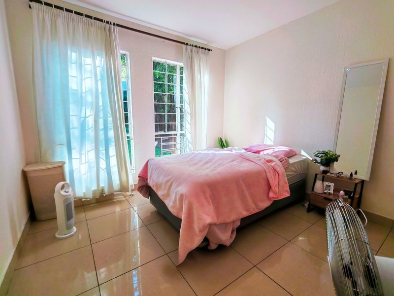 A bright bedroom featuring large windows with natural light, tiled flooring, and neutral wall finishes, offering a clean and comfortable living space.