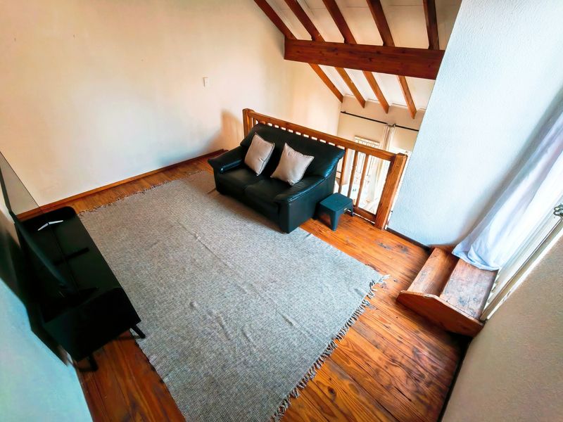 A loft-style living area featuring exposed timber rafters, wooden flooring, and a timber balustrade overlooking the lower level.