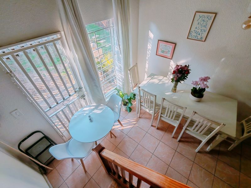 A bright dining area featuring tiled flooring, large windows with natural light, and direct access to the exterior via a security gate.