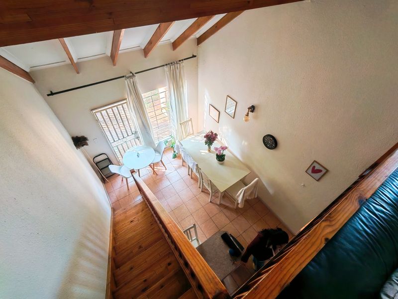 An elevated view of an open-plan dining area featuring exposed timber ceiling beams, tiled flooring, and direct access to an outdoor space via a sliding door.