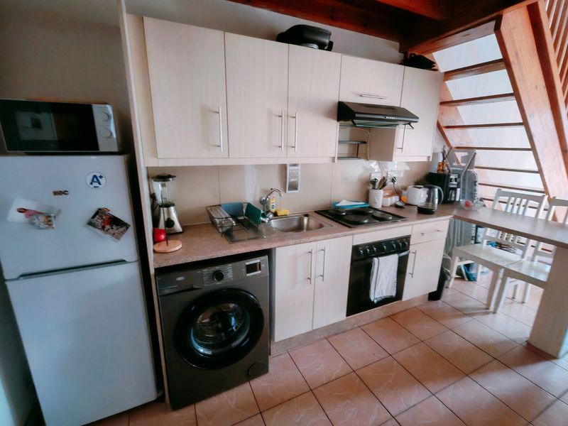 Compact kitchen featuring light-toned cabinetry, integrated oven and hob, tiled flooring, and an adjacent wooden staircase.