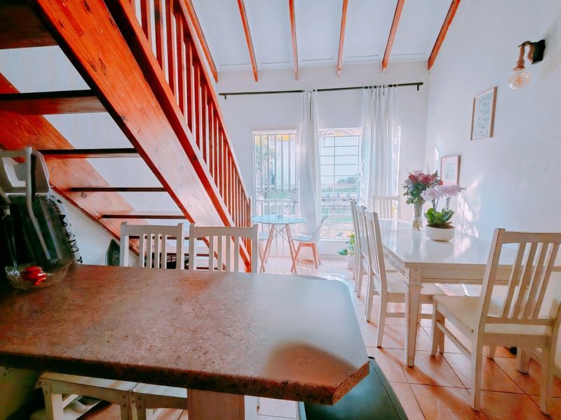 Open-plan living and dining area featuring a prominent wooden staircase, exposed timber ceiling beams, and tiled flooring with access to an outdoor patio.