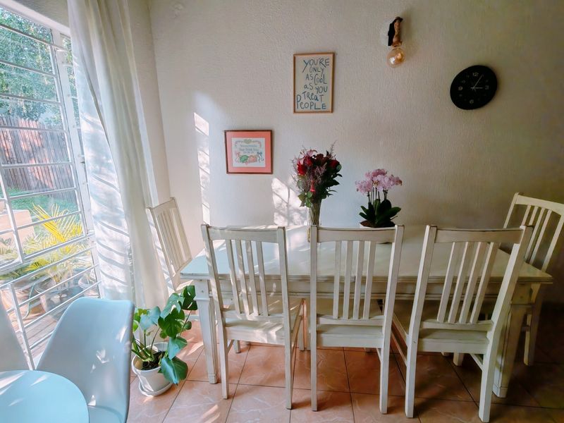 A bright dining area featuring tiled flooring and large windows with security bars, providing natural light and a view of the garden.
