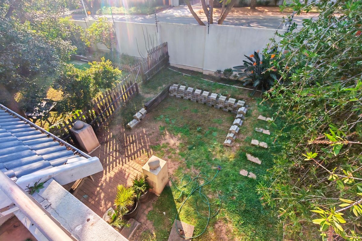 An elevated view of a rear garden featuring a paved patio area, a small retaining wall, and a lawn with a stepped stone path.