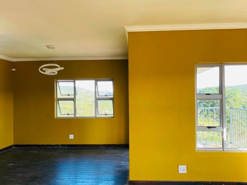 Spacious, empty living area featuring dark hardwood flooring, mustard-toned walls, modern circular pendant lighting, and large windows with scenic views.