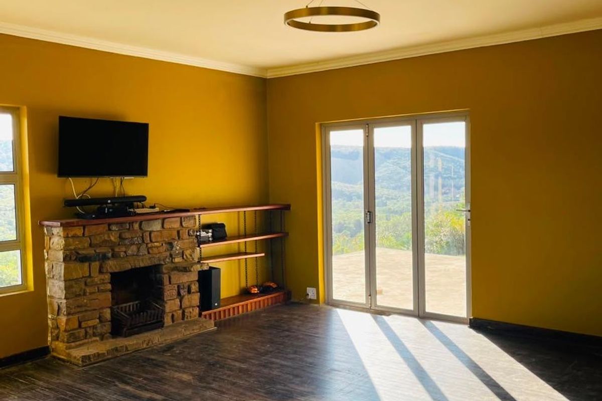 Spacious living room featuring a rustic stone fireplace, timber flooring, and large folding doors that open to scenic landscape views.