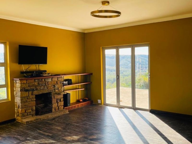 Spacious living room featuring a rustic stone fireplace, timber flooring, and large folding doors that open to scenic landscape views.