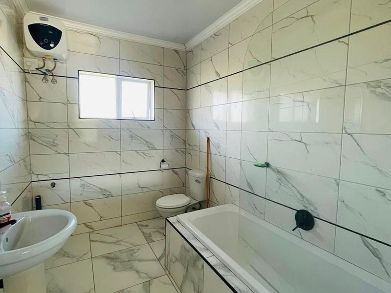 A clean, modern bathroom featuring marble-look wall and floor tiles, a pedestal basin, a bathtub, and an integrated electric water heater.