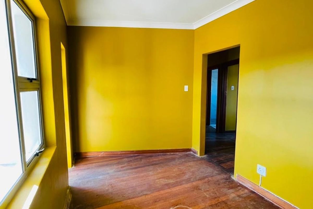 An empty bedroom featuring original hardwood flooring, aluminium window frames, and cove cornicing, ready for renovation or restyling.