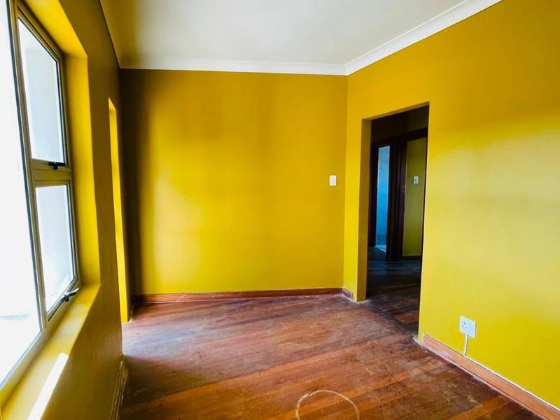 An empty bedroom featuring original hardwood flooring, aluminium window frames, and cove cornicing, ready for renovation or restyling.