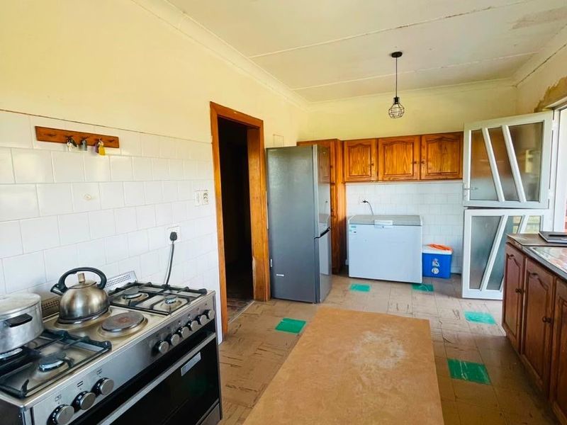 A dated kitchen featuring wooden cabinetry, a gas stove, tiled backsplash, and a stable door, requiring cosmetic updates to improve its overall condition.