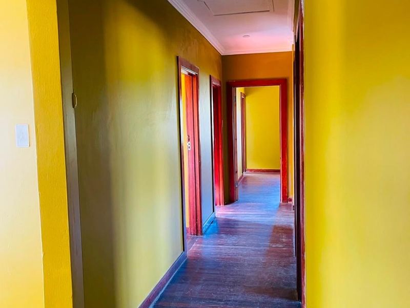 A long interior hallway featuring original hardwood flooring, yellow painted walls, and traditional wooden door frames leading to multiple rooms.