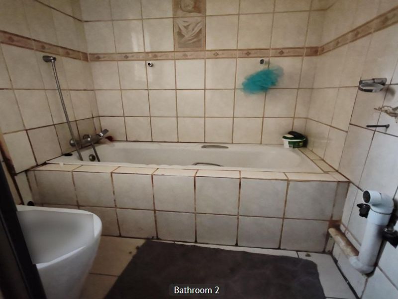 A dated bathroom featuring a built-in bathtub with shower mixer, requiring significant maintenance and cosmetic updates to the wall tiling and exposed plumbing fixtures.