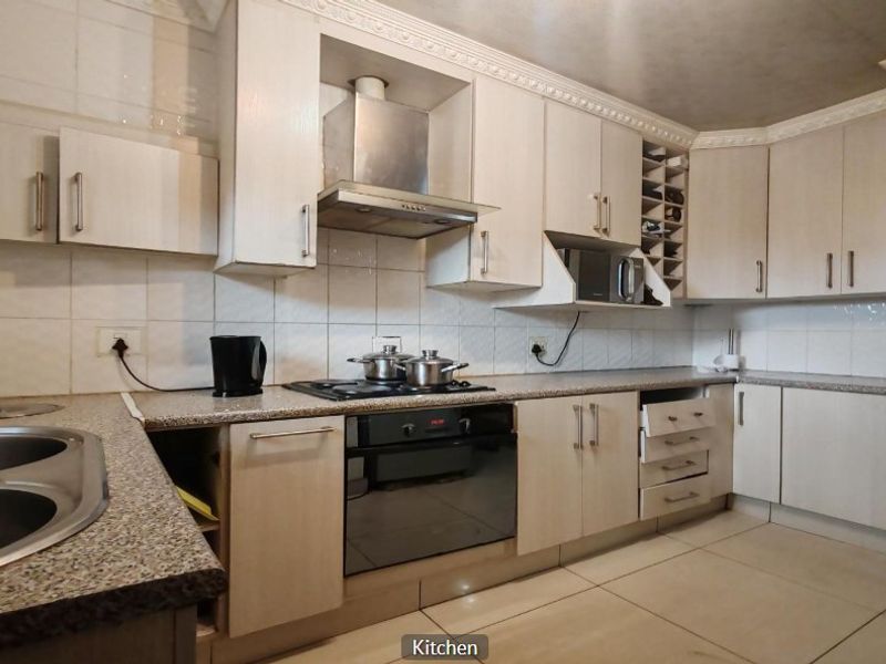 A functional kitchen featuring light-toned cabinetry, granite countertops, built-in appliances, and tiled finishes, offering a practical layout with potential for cosmetic updates.