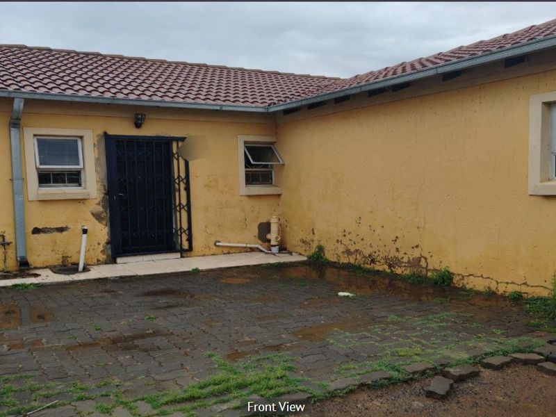 Rear exterior view of the property featuring a paved courtyard, security gate, and tiled roof, showing signs of significant exterior maintenance required.