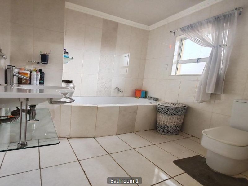 A functional bathroom featuring a built-in bathtub, wall-mounted basin, and toilet with neutral tiled finishes throughout.