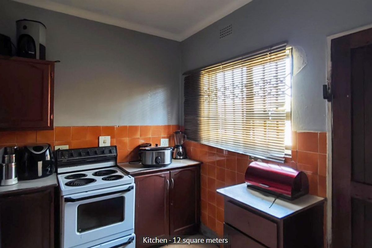 A functional kitchen featuring dark wood cabinetry, orange tiled splashbacks, and a freestanding stove, with some minor plaster damage visible near the window.