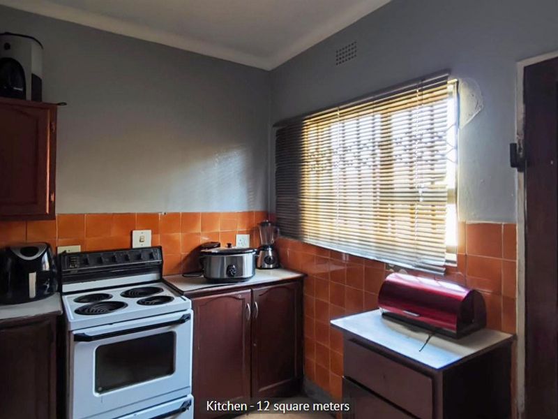 A functional kitchen featuring dark wood cabinetry, orange tiled splashbacks, and a freestanding stove, with some minor plaster damage visible near the window.