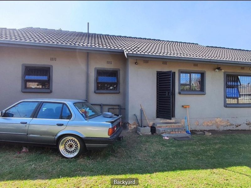 Rear exterior view of the house featuring a tiled roof, security bars on windows, and a rear access door with concrete steps.