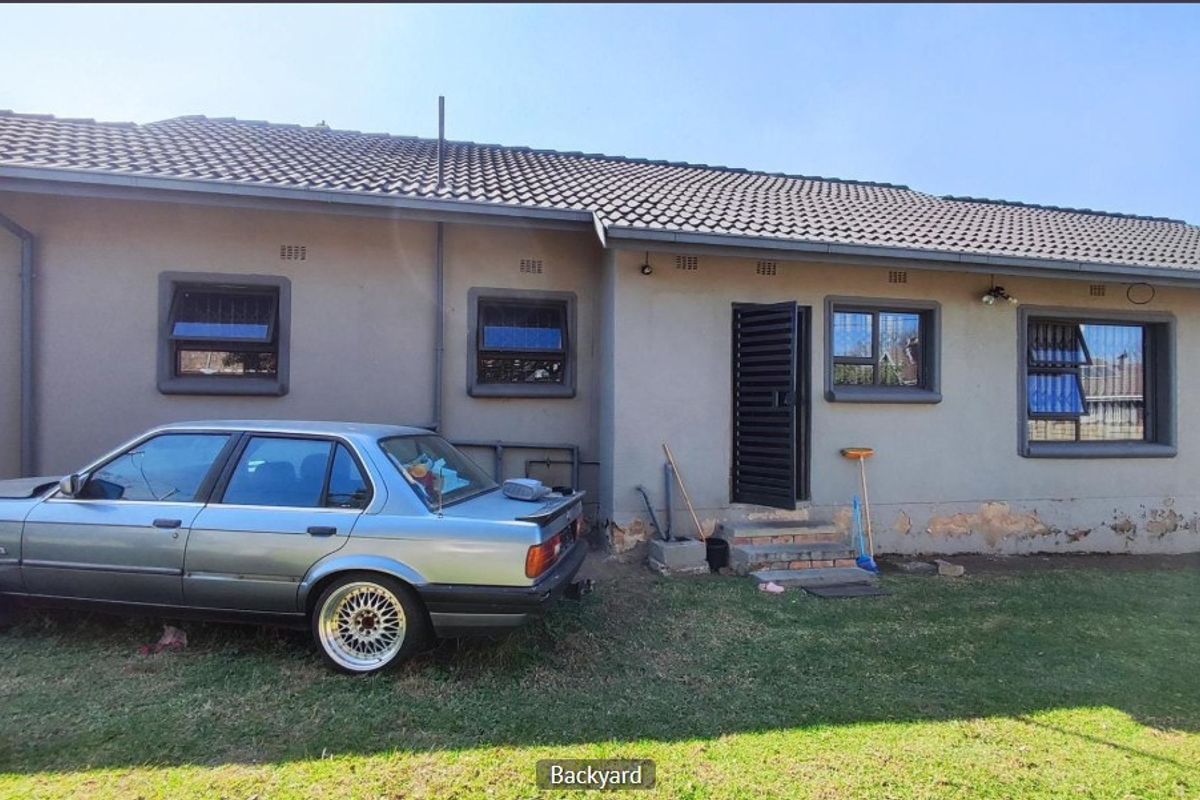 Rear exterior view of the house featuring a tiled roof, security bars on windows, and a rear access door with concrete steps.