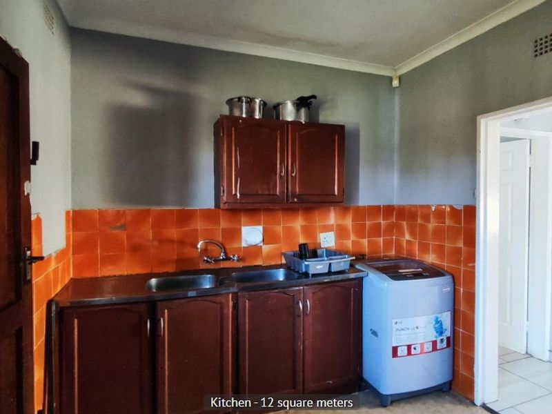 A compact kitchen featuring wooden cabinetry, a double stainless steel sink, and orange tiled splashbacks, offering potential for a modern renovation.