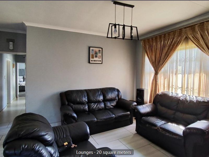 A spacious living room featuring tiled flooring, neutral wall tones, and a central pendant light fixture, providing a comfortable and functional family area.