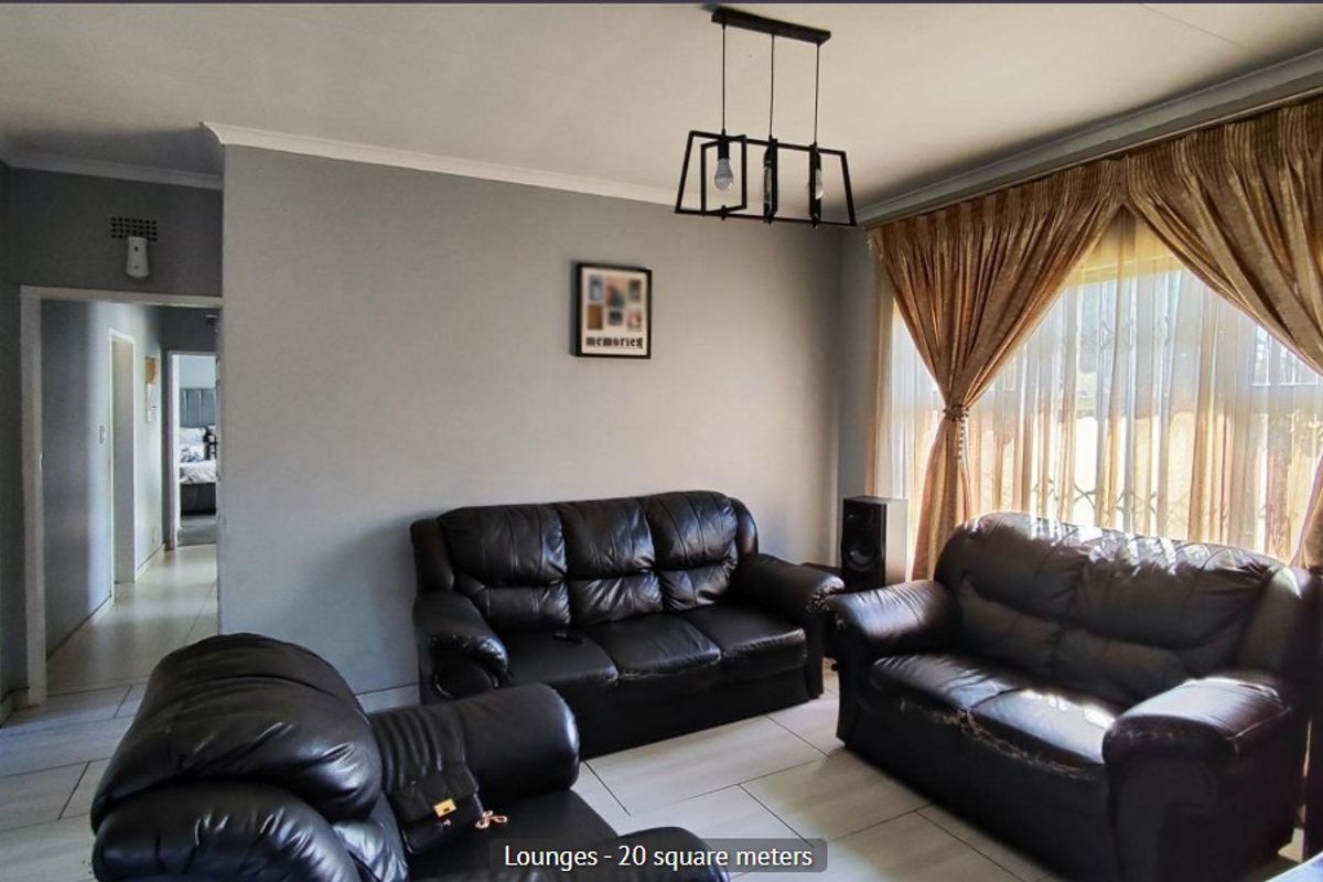 A spacious living room featuring tiled flooring, neutral wall tones, and a central pendant light fixture, providing a comfortable and functional family area.