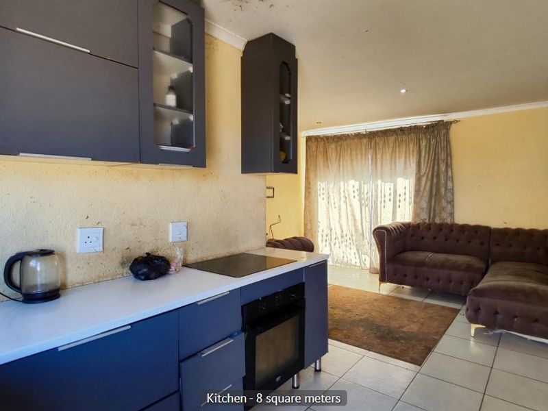 Open plan kitchen and living area featuring dark cabinetry, built-in oven, electric hob, and tiled flooring with access to the outdoor area.