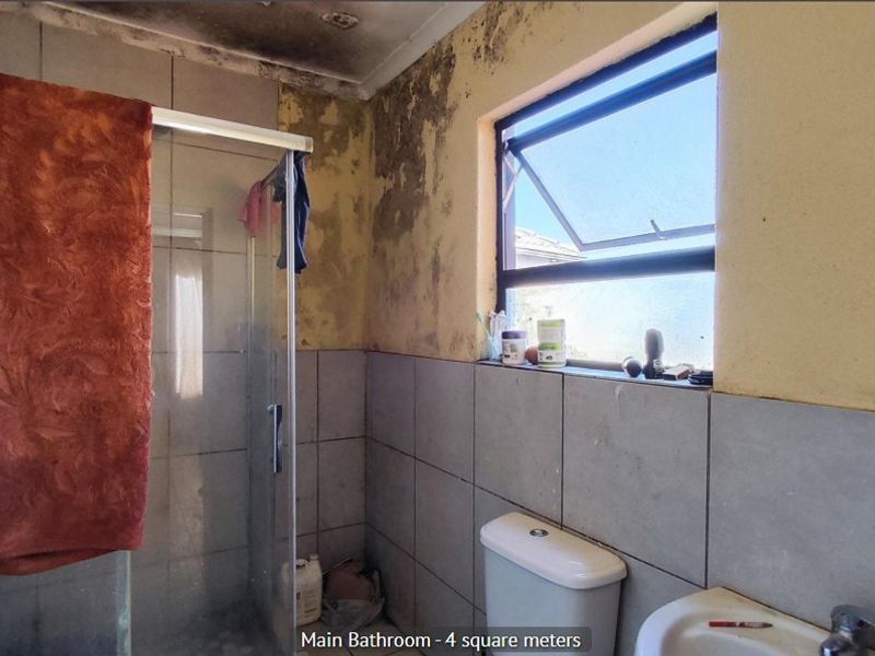 A compact bathroom featuring a shower enclosure, toilet, and washbasin, currently requiring significant maintenance and repair due to visible wall and ceiling damage.