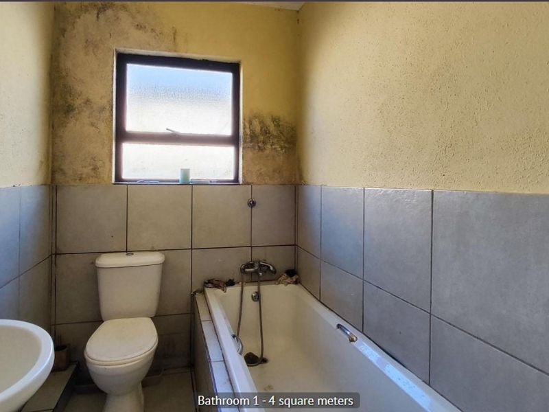 A compact bathroom featuring a bathtub, toilet, and pedestal basin, currently requiring maintenance and cosmetic updates to address visible wall staining.