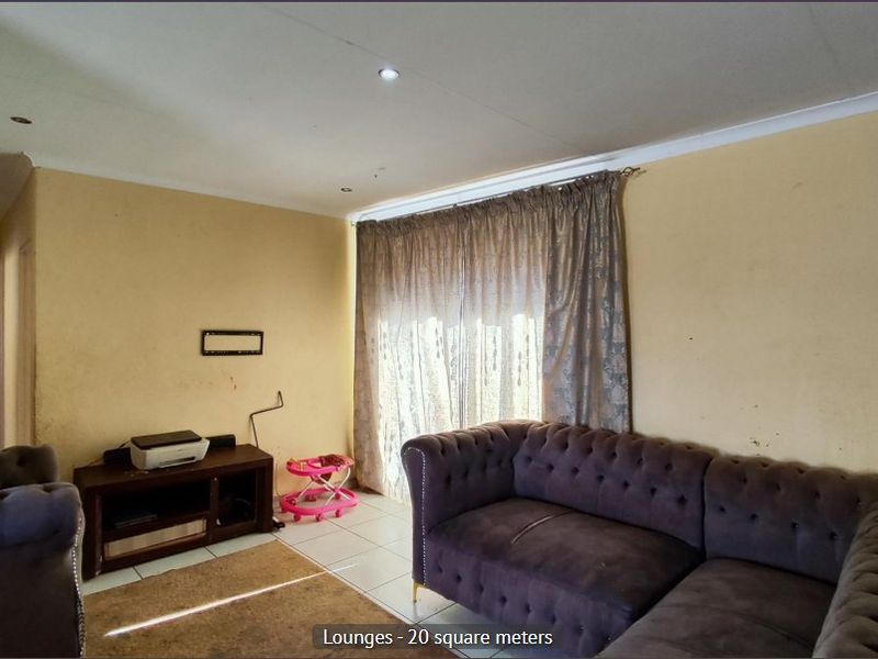 A living room featuring tiled flooring, recessed downlighting, and a sliding glass door. The walls show signs of wear and require repainting.