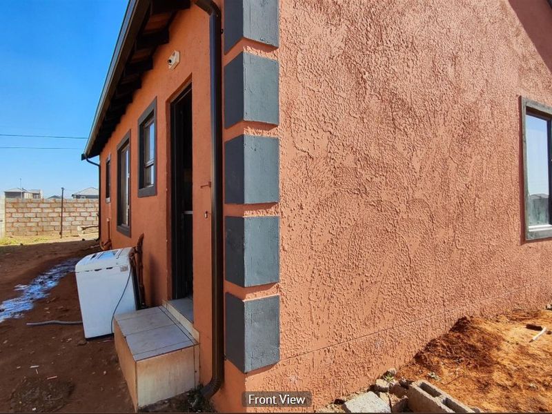 Side view of a house featuring a textured stucco facade with contrasting corner detailing, aluminium window frames, and an entrance step.
