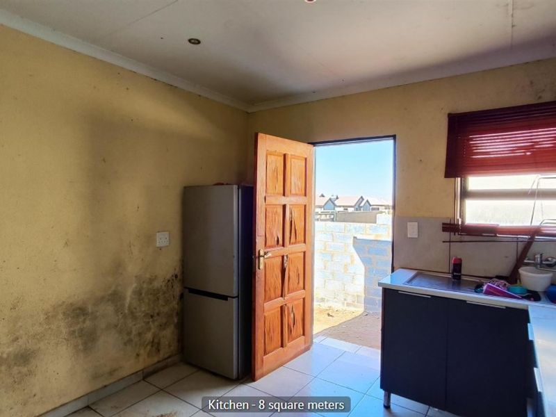 A compact kitchen featuring tiled floors, built-in cabinetry, and a sink, requiring significant maintenance and cosmetic updates to address wall damage.