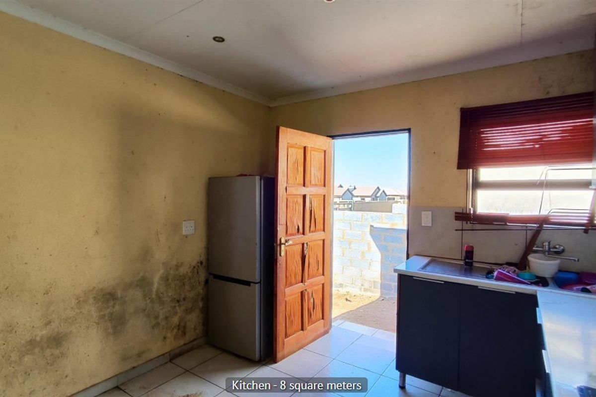 A compact kitchen featuring tiled floors, built-in cabinetry, and a sink, requiring significant maintenance and cosmetic updates to address wall damage.