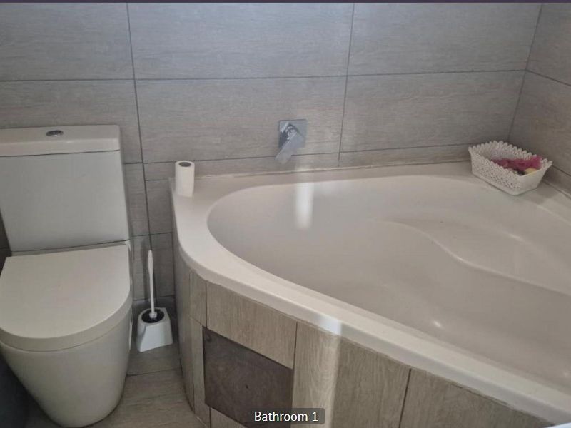 A functional bathroom featuring a corner bathtub with wall-mounted mixer tap and a modern toilet, finished with neutral wall tiling.