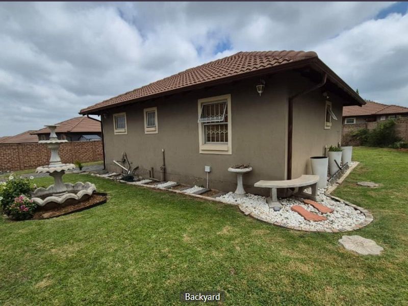 Rear view of the property featuring a well-maintained lawn, brick boundary walls, and established garden landscaping with a stone fountain.