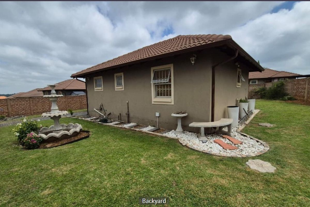Rear view of the property featuring a well-maintained lawn, brick boundary walls, and established garden landscaping with a stone fountain.