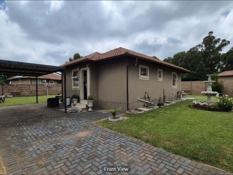 A well-maintained residential property featuring a paved driveway, a covered carport, and a landscaped garden with a decorative water fountain.