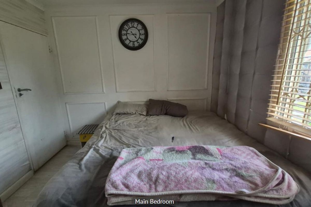 A bedroom featuring wainscoting wall detailing, laminate flooring, and venetian blinds. The room requires cosmetic updates to improve its overall condition and appeal.