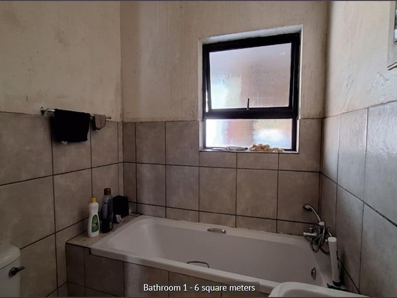 A compact bathroom featuring a bathtub, toilet, and tiled wall finishes, requiring cosmetic updates to improve the overall condition.
