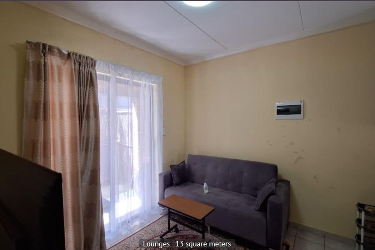 A compact living room featuring tiled flooring, a sliding glass door providing natural light, and a wall-mounted electrical distribution board.