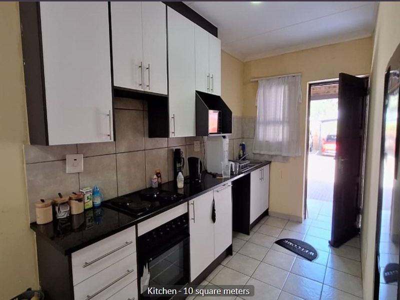 Compact kitchen featuring modern two-tone cabinetry, granite countertops, built-in oven and hob, tiled backsplash, and direct access to the exterior.