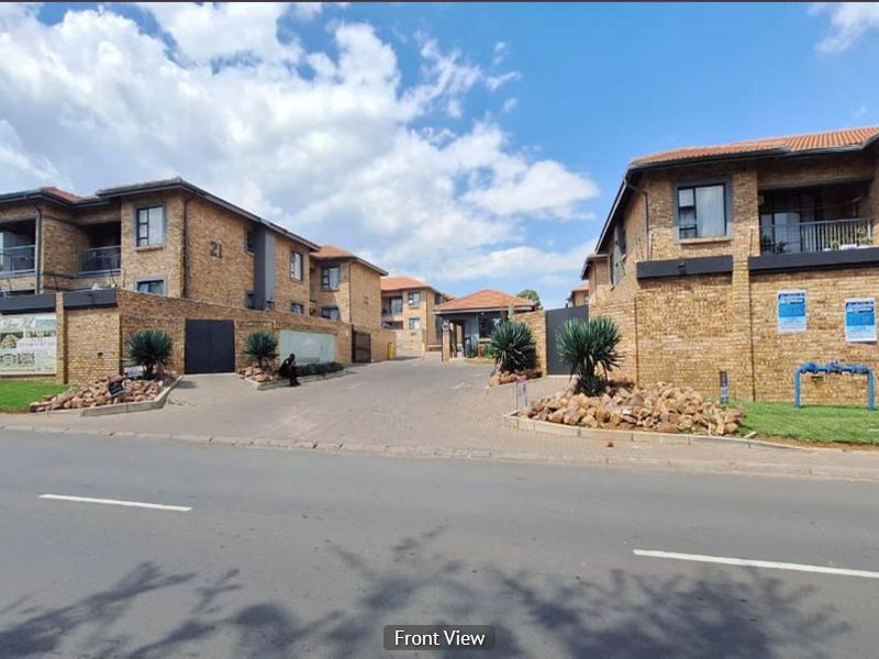 Street view of the apartment complex entrance featuring face brick buildings, paved driveway, and secure perimeter walling.