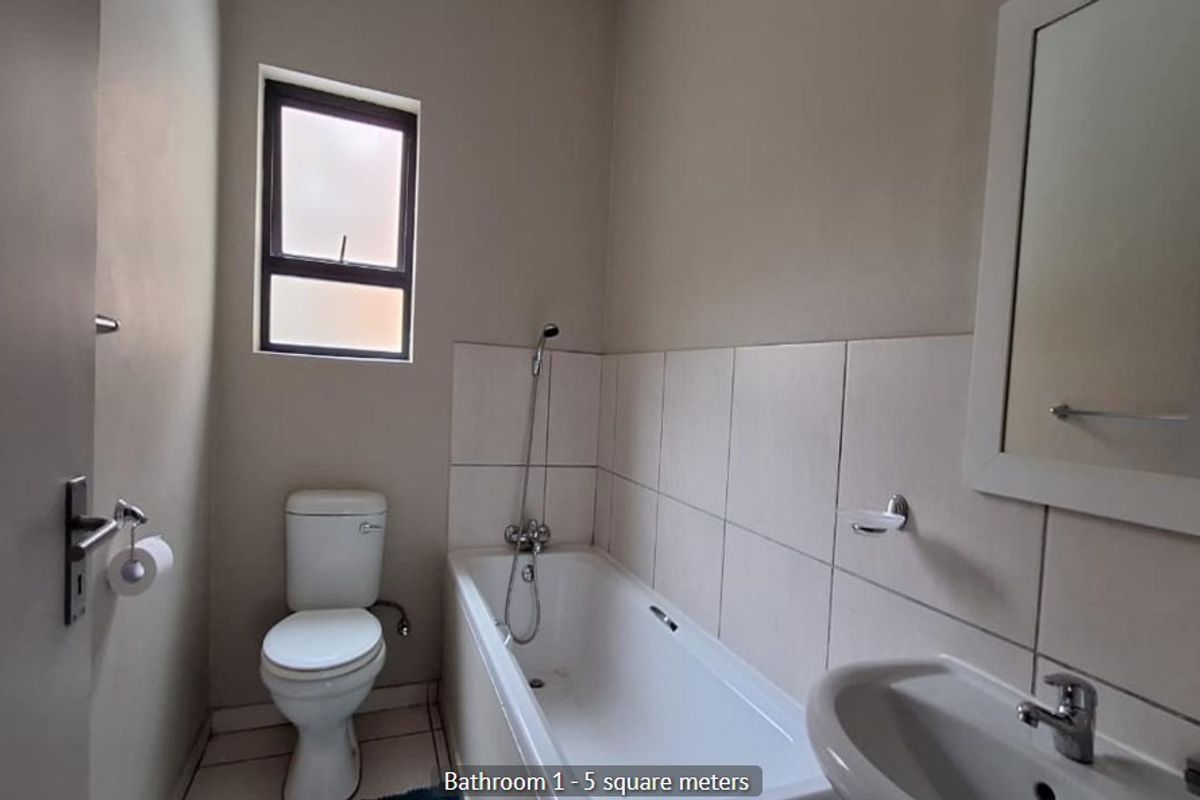 A functional bathroom featuring a bathtub, pedestal basin, and toilet with neutral wall tiles and flooring.