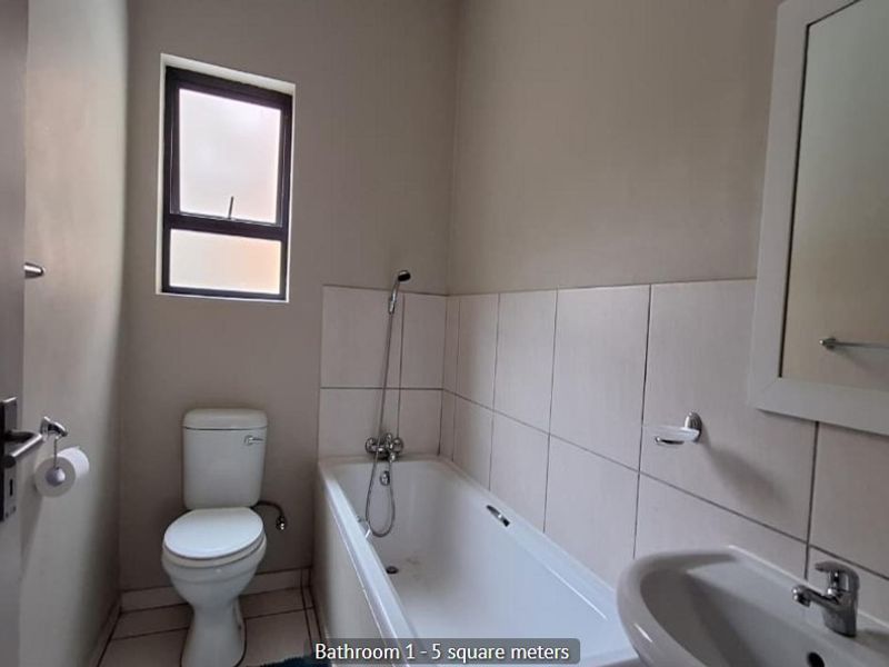 A functional bathroom featuring a bathtub, pedestal basin, and toilet with neutral wall tiles and flooring.
