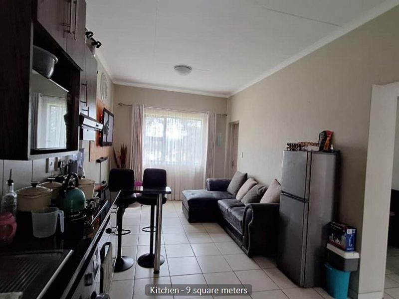 Open-plan living area featuring a compact kitchen with built-in cabinetry and a breakfast bar, seamlessly flowing into the lounge space with tiled flooring.