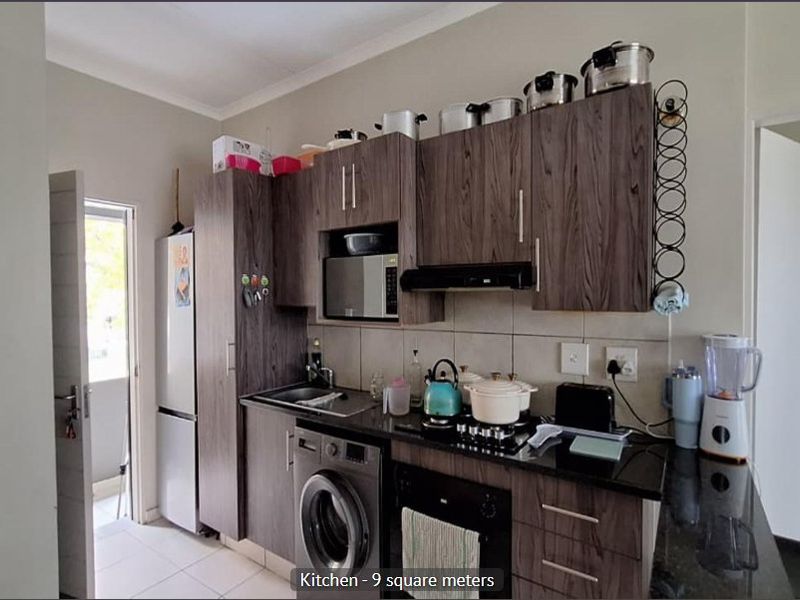 Compact kitchen featuring dark wood-look cabinetry, granite countertops, built-in oven, gas hob, and integrated extractor fan with tiled backsplash.