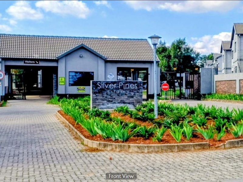 The entrance to Silver Pines Estate featuring a paved driveway, security gatehouse, and well-maintained landscaped garden beds.