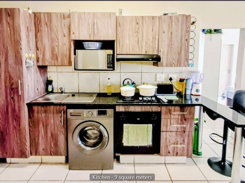 Compact kitchen featuring wood-look laminate cabinetry, granite countertops, built-in oven, hob, extractor fan, and integrated laundry appliance space.
